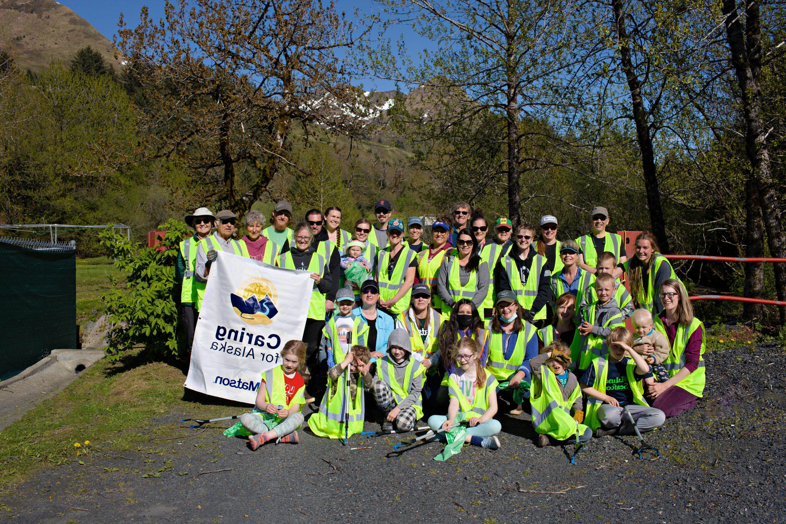 Volunteers wearing their yellow safety vests pose for a group picture with a Caring For Alaska banner.